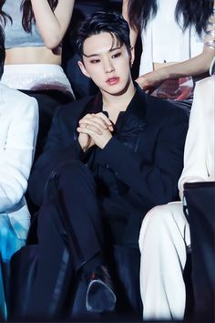 the young man is sitting in front of other people at an event with his hands together