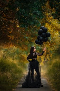 a woman is holding black balloons in the middle of a road with trees behind her