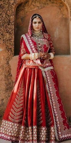 a woman in a red and gold wedding dress standing next to a wall with her hands on her hips