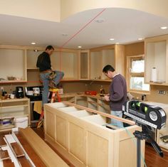 two men are working in a kitchen with wood cabinets and drawers on the counter tops