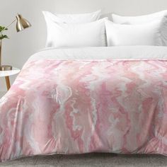 a bed with pink and white comforter on top of it next to a lamp