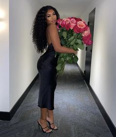 a woman in a black dress is holding a large bouquet of roses and looking at the camera