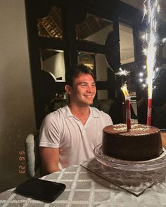 a man sitting in front of a chocolate cake with two lit candles on top of it