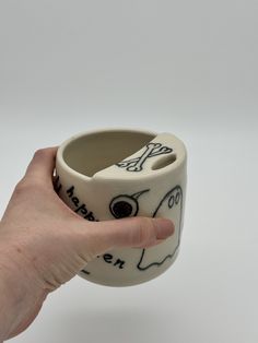 a hand is holding a ceramic cup with writing on it