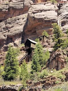 an old wooden cabin on the side of a rocky cliff with trees growing out of it