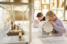 two people looking at items on display in a glass case with wooden figures behind them