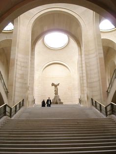 two people are standing at the top of some stairs in a large building with arches