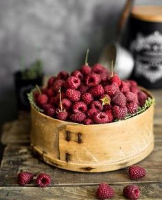 a wooden bowl filled with raspberries on top of a table