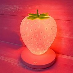 a strawberry shaped light sitting on top of a wooden table next to a pink wall