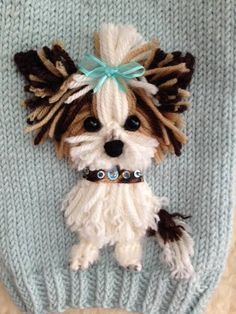 a knitted dog wearing a blue bow on it's head, sitting on top of a sweater