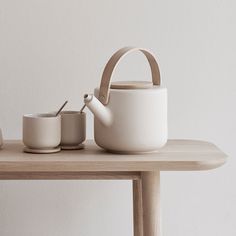 two cups and a teapot on a table with a white wall in the background