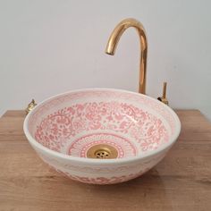 a pink and white bowl sink sitting on top of a wooden counter next to a faucet