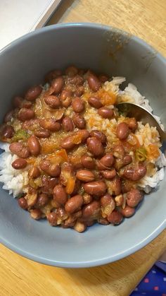 a blue bowl filled with rice and beans on top of a wooden table next to a spoon