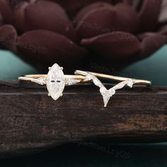 two gold rings with white diamonds on them sitting on a piece of wood next to a flower