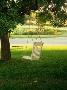 a white chair hanging from a tree in the grass