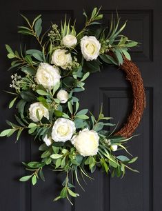 a wreath with white flowers and greenery hanging on a door