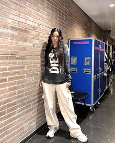 a woman standing in front of a brick wall next to a blue locker with letters on it