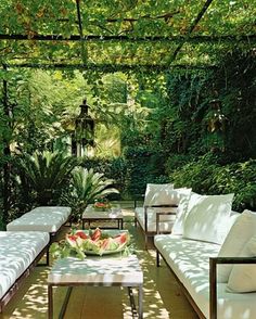 an outdoor living area with white furniture and trees in the background, including two couches and a coffee table