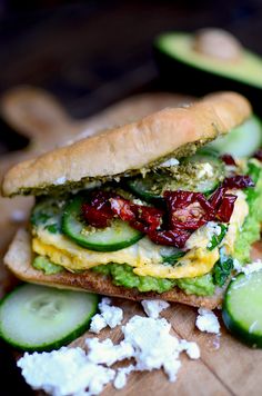 a sandwich with cucumbers, cheese and other toppings on a cutting board