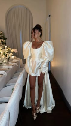 a woman in a white dress standing next to a table