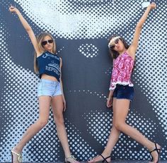 two young women standing next to each other in front of a wall