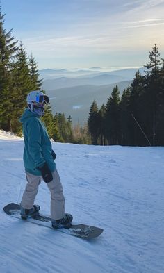 a person riding a snowboard on top of a snow covered slope with trees in the background