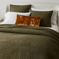 a bed with green bedspread and pillows on top of it in a bedroom