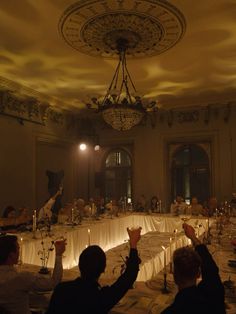 a group of people raising their glasses in the air at a dinner table with candles on it