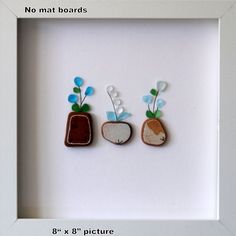 three small rocks with flowers in them are mounted in a white frame on the wall