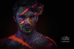 a man with his face covered in colored powder and black background is looking at the camera