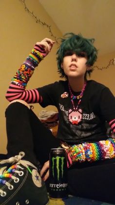 a boy with green hair sitting on the floor next to his shoes and wearing colorful bracelets