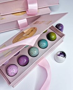 an open box with six different colored eggs in it and pink ribbon on the side