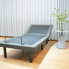 a bed sitting on top of a hard wood floor next to a white table with a plant in it