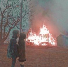 two people standing in front of a house on fire