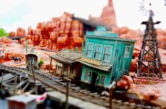 an image of a model train set with buildings and people on the tracks in front of them