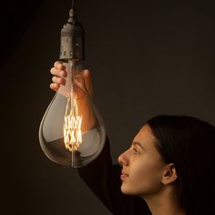 a woman holding a light bulb up to her face and looking at it in the air