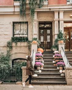 a woman is walking down the steps in front of a building with flowers and pumpkins