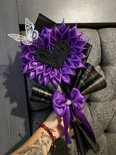 a purple sunflower bouquet with black ribbon and butterflies on the top is being held by a woman's arm