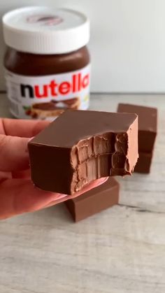 a hand holding a piece of chocolate with nutella in the background