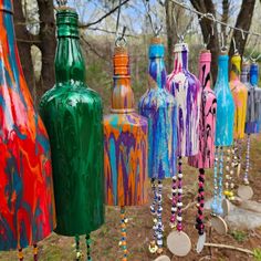 many colorful bottles are hanging from a line in the woods with beads and necklaces attached to them