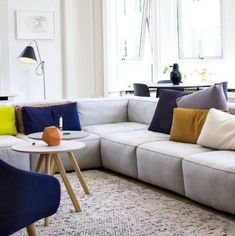 a living room with white couches and colorful pillows on the sofa, next to a coffee table