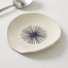 a white dish with a black design on it and a spoon next to it that says west elm