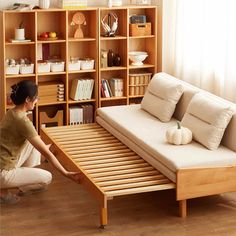 a woman kneeling on the floor next to a bed with a wooden frame and mattress