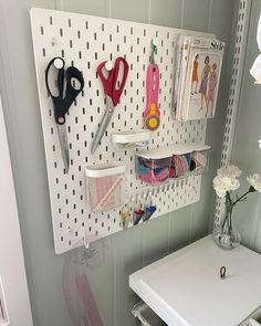 a white desk with scissors and other crafting supplies on the pegboard next to it