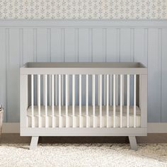 a white crib in front of a blue wall with flowers on it and a basket next to it