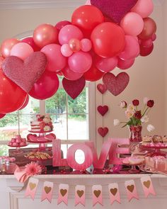 a table topped with lots of pink and red balloons next to a sign that says love