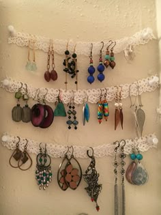 there are many different earrings hanging on the wall with white lace and beads attached to it