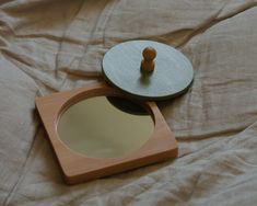 a wooden mirror sitting on top of a bed next to a round mirror with a wooden lid