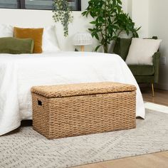 a wicker storage box sits on the floor in front of a bed with white sheets and pillows