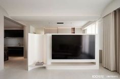 a flat screen tv sitting on top of a white shelf in a living room next to a window